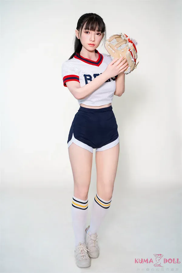A girl wearing a sports uniform with a cropped top and shorts, holding a baseball glove, standing against a plain background.