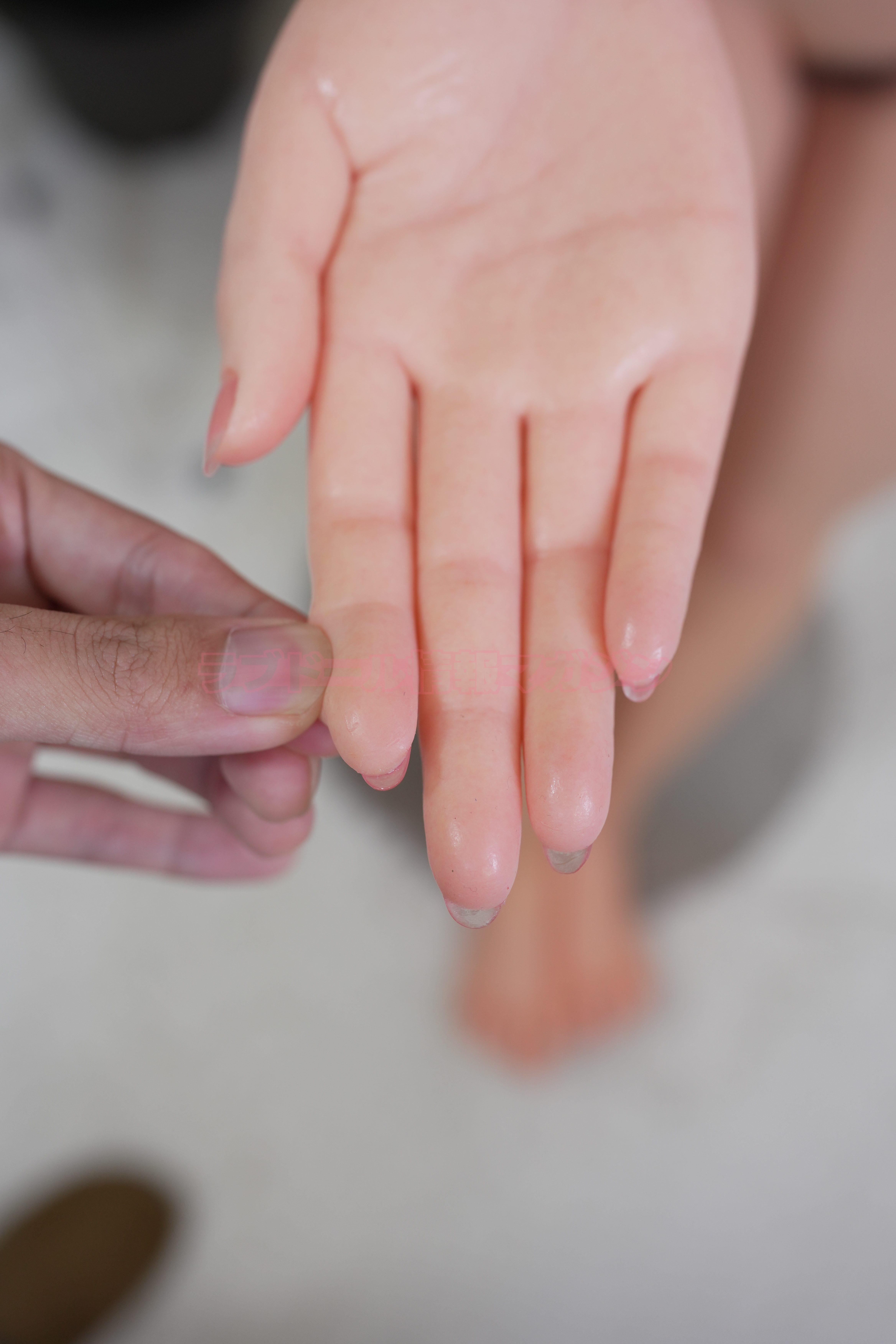 A hand of a love doll being gently pressed, showing realistic silicone texture.