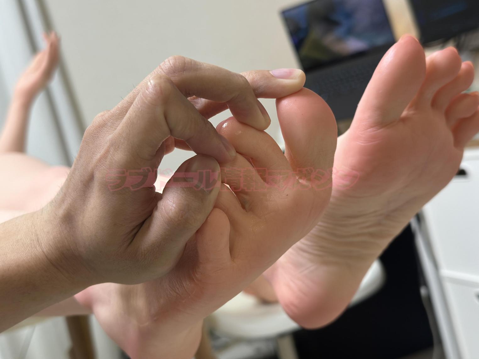 A close-up image of a hand gently squeezing the toes of a realistic model foot, showcasing the detailed skin texture and realistic features.