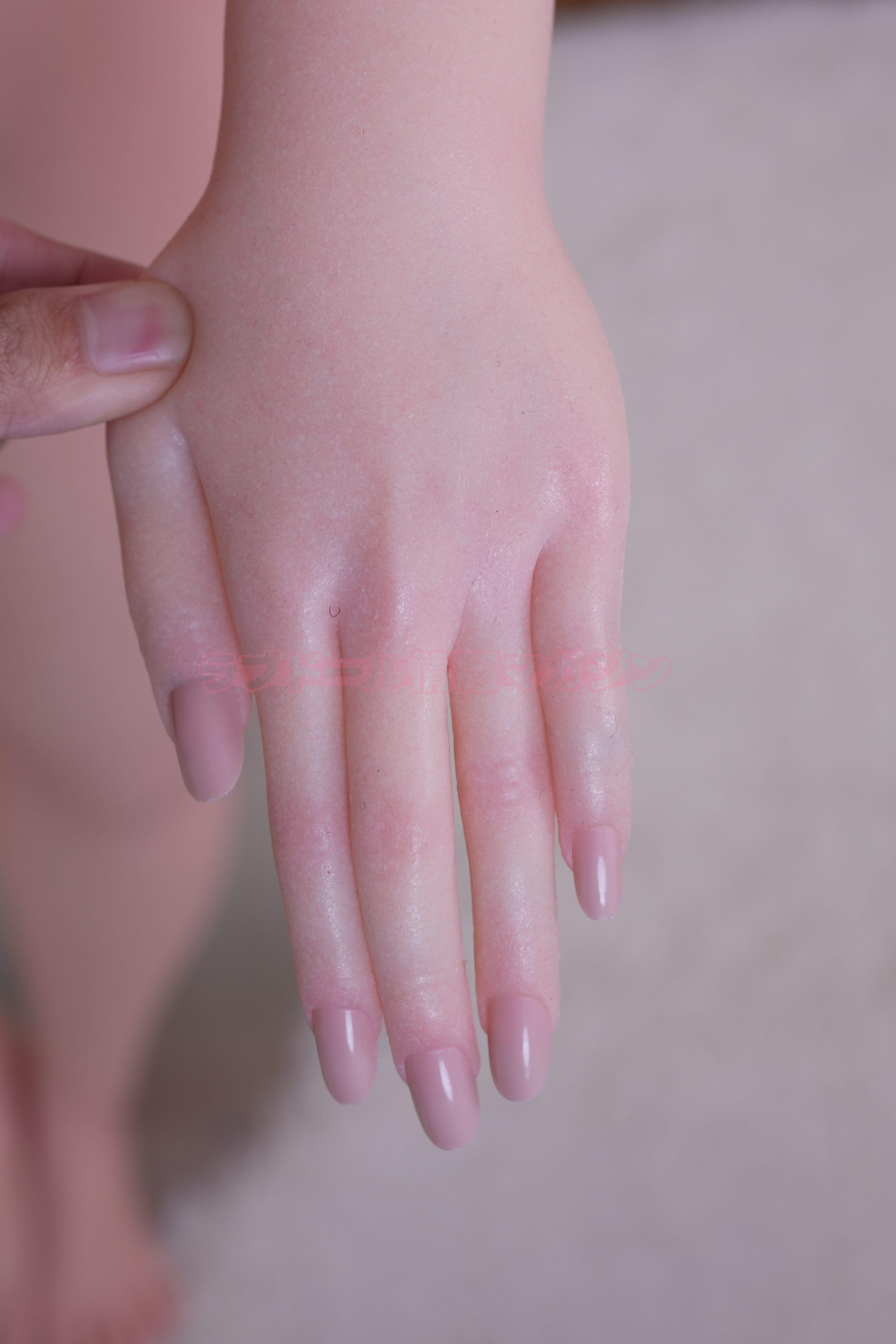 A close-up of a realistic silicone hand with long, manicured nails in a natural skin tone, being gently held. The texture appears smooth and lifelike.